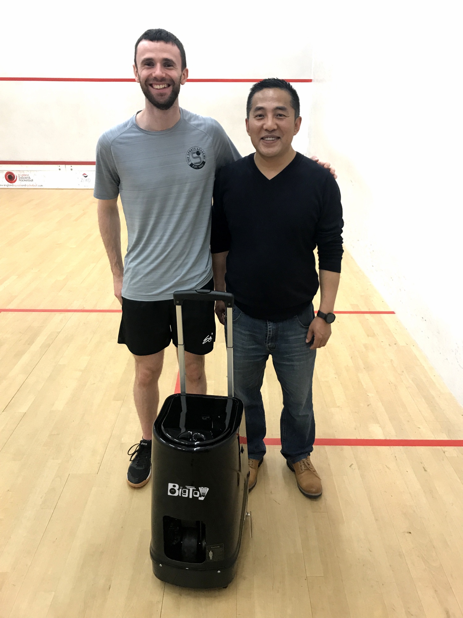 Coach standing with squash ball machine on court